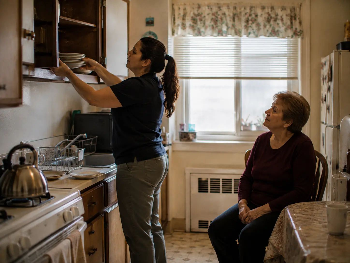 An occupational therapist moving dishes from a high cupboard down to the counter in a New York apartment kitchen