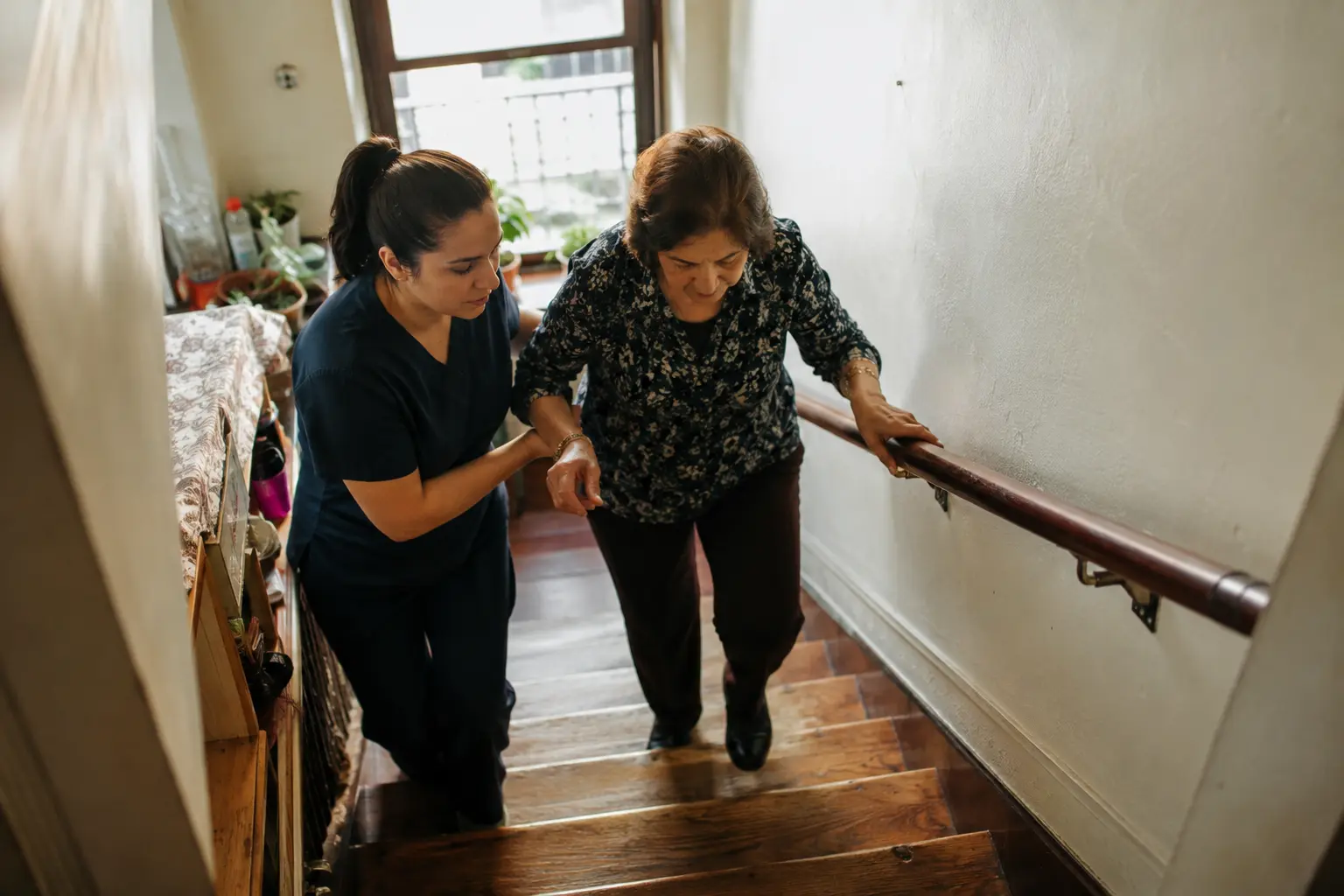 A physical therapist steadying an older woman on the stairs of her Brooklyn walk-up building