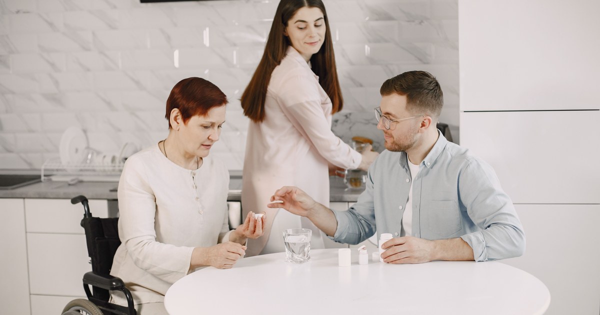 Woman in a wheelchair being helped with medication by family at home