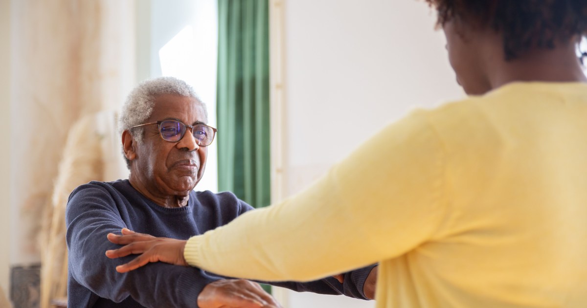 Caregiver assisting an elderly man with balance exercises at home