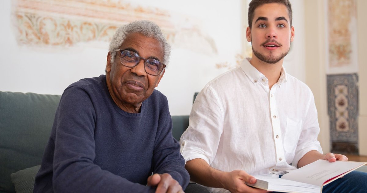 Home care aide and an older man looking through a book together on a sofa