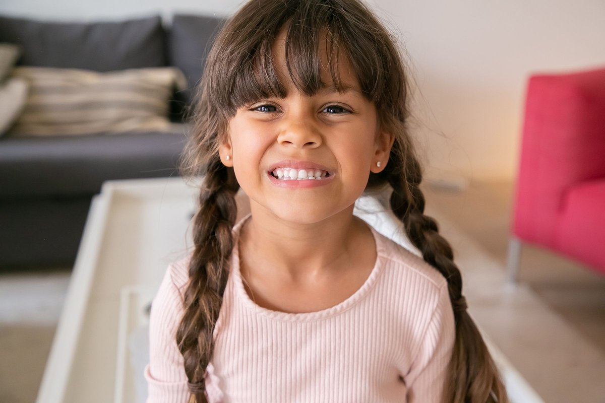 Smiling school-age girl with long braids sitting at home