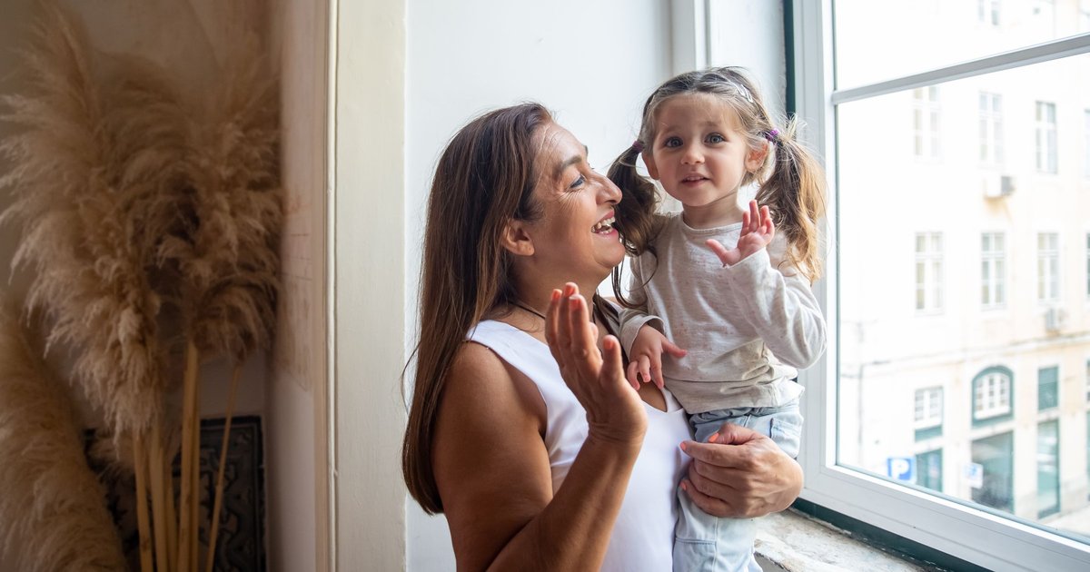Smiling woman holding a little girl by a sunny window as they play together