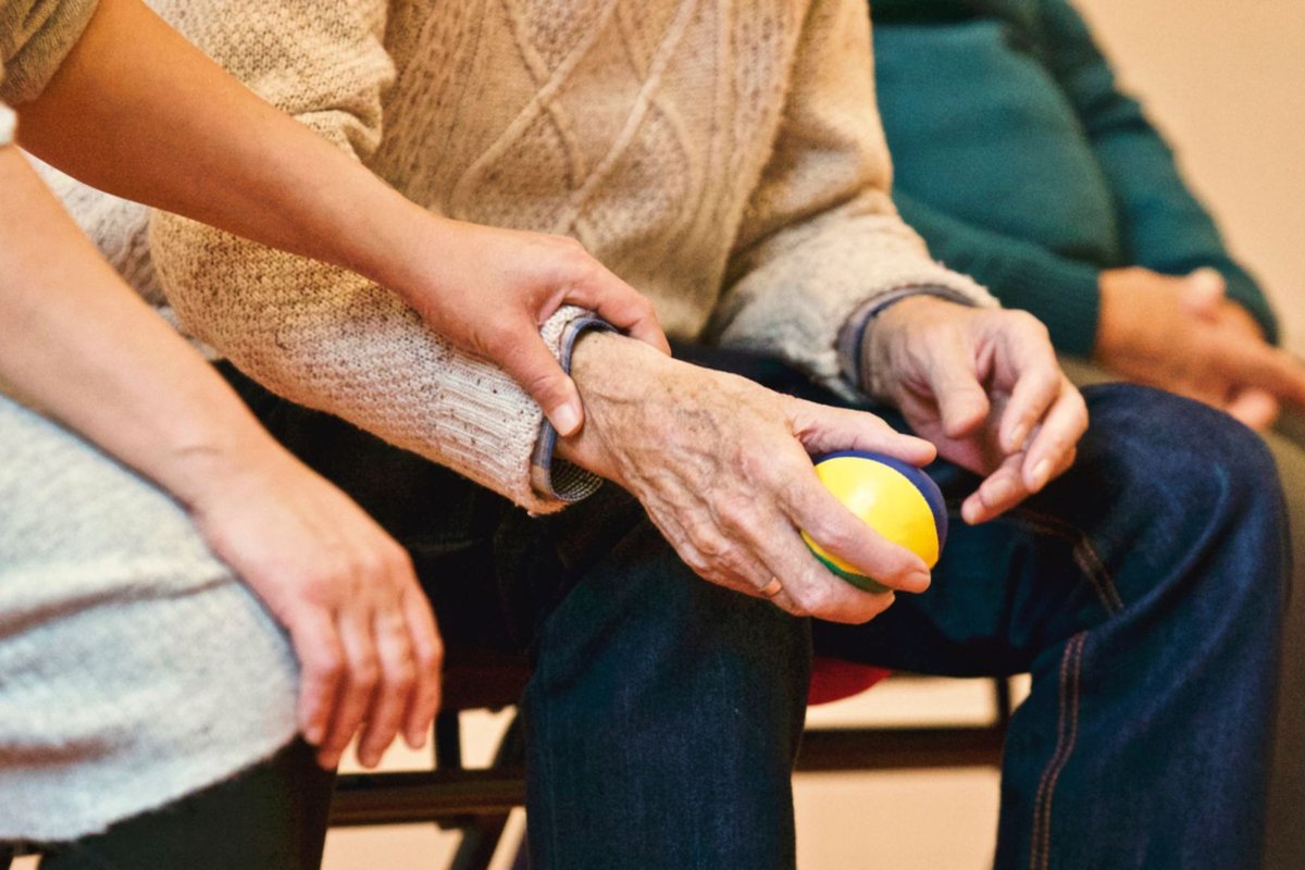 Caregiver's hands resting on an older person's hands holding a soft ball