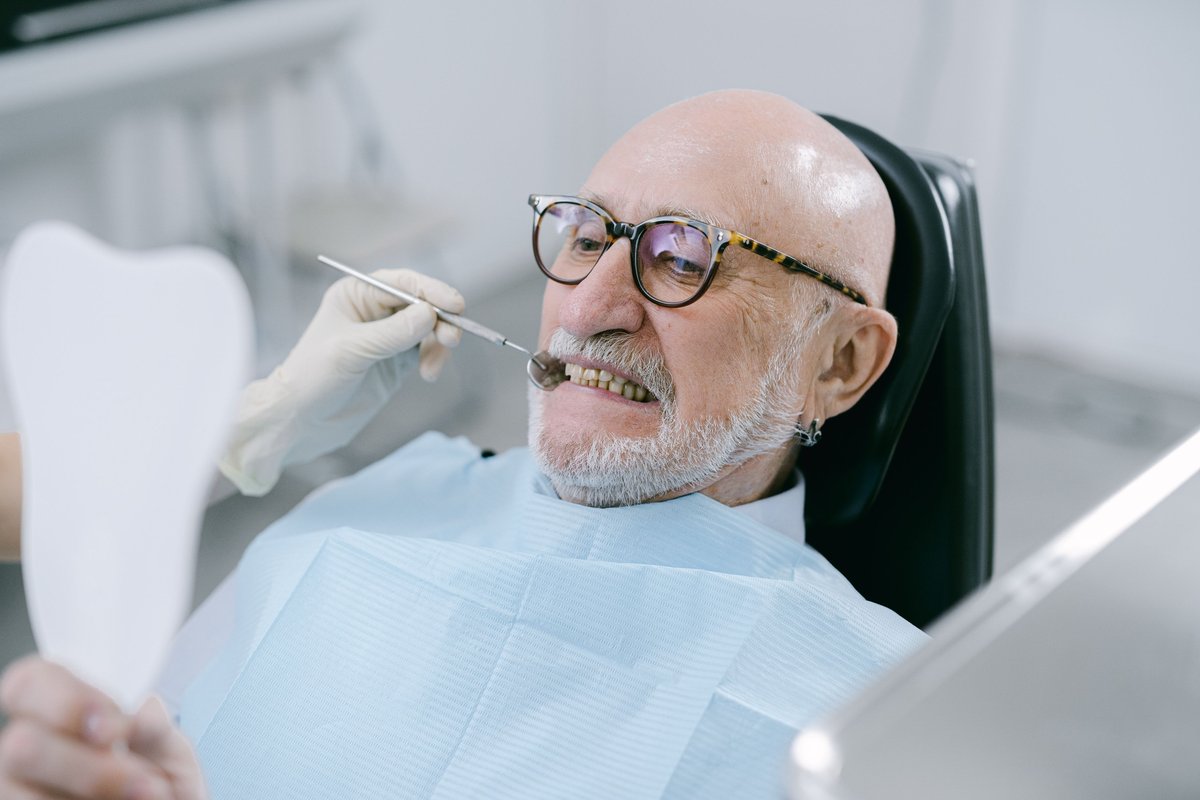 Older man in the dental chair holding a hand mirror during a dental checkup