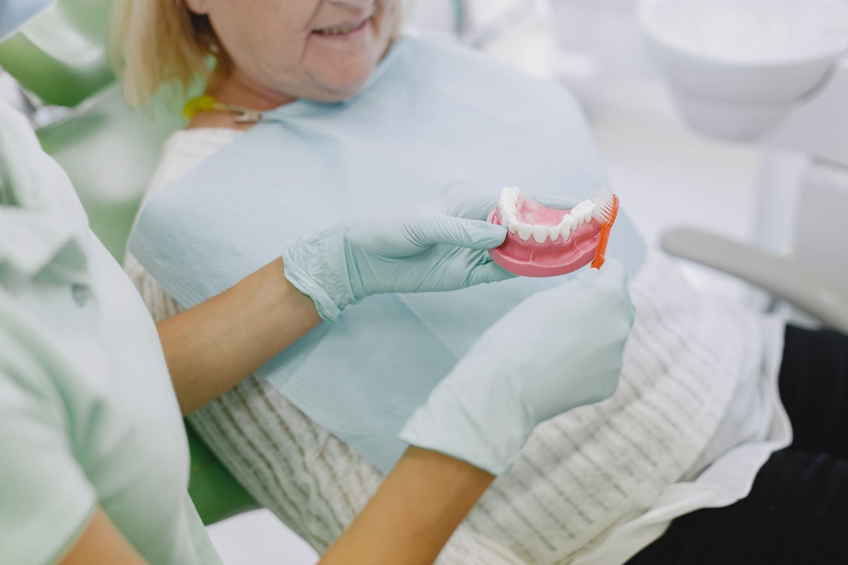 Dentist holding a denture model and toothbrush while explaining care to an older patient