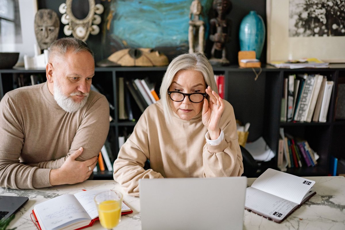 Older couple at a marble counter looking at a laptop beside open planners