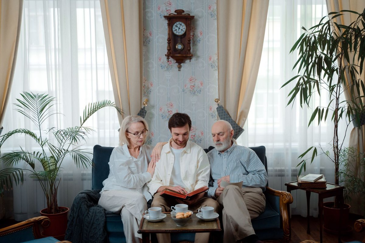 Elderly couple and their adult son sitting on a sofa with tea, looking at an album