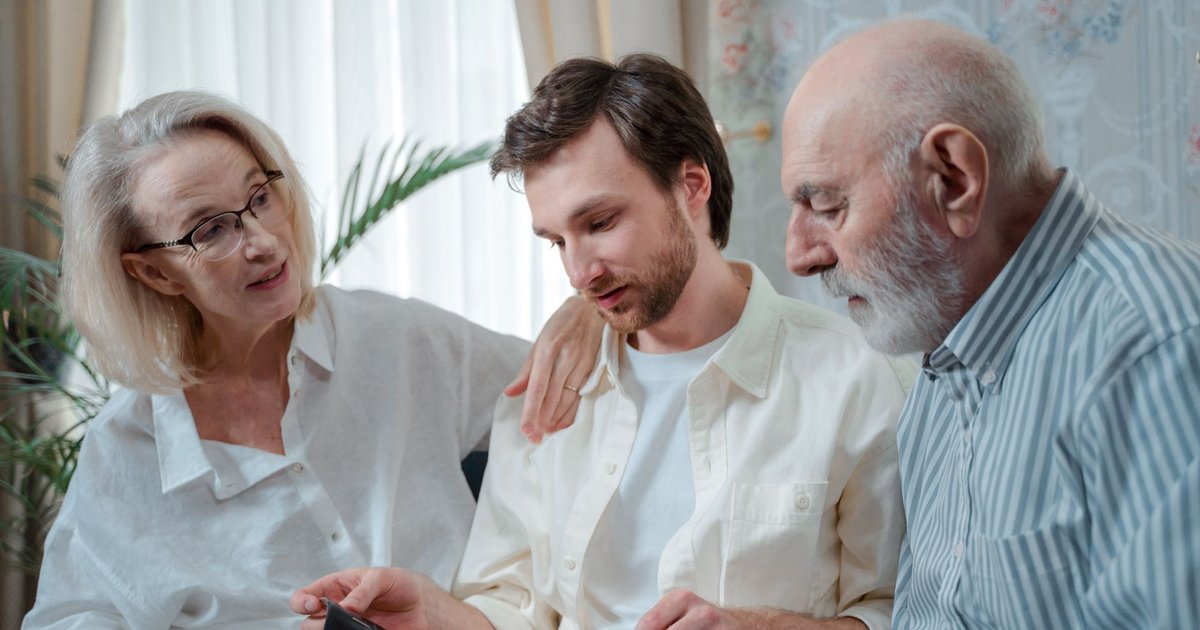 Older couple sit beside their adult son on a sofa, talking together at home