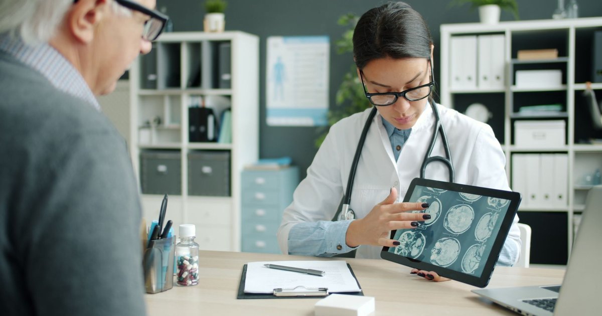 Doctor explaining brain scans on a tablet to an older patient during a memory evaluation