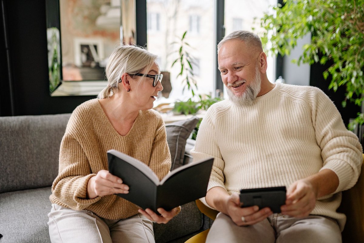Older couple on a sofa looking through a notebook and a tablet while planning together