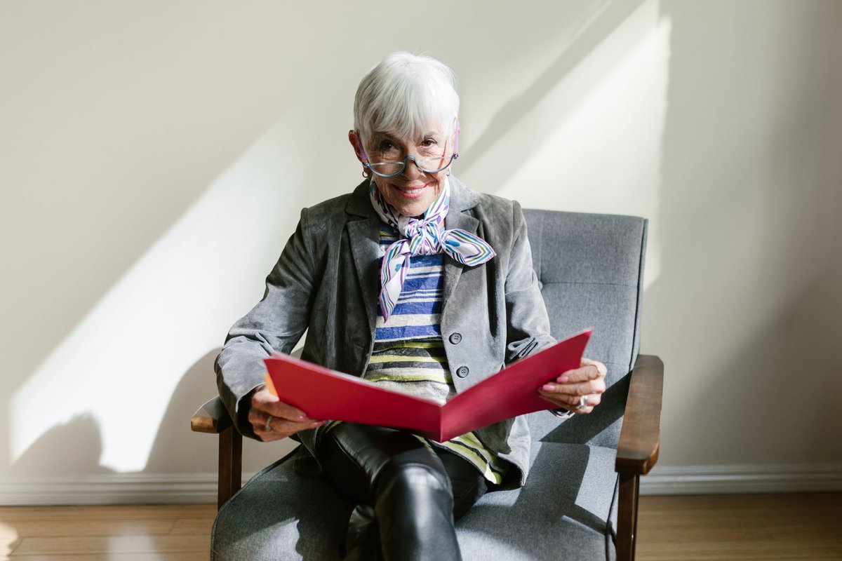 Smiling senior woman in a gray armchair holding an open red folder of documents
