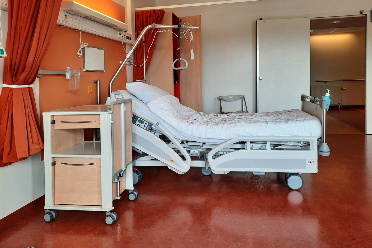 Adjustable hospital-style bed with an overhead trapeze bar and a rolling bedside cabinet
