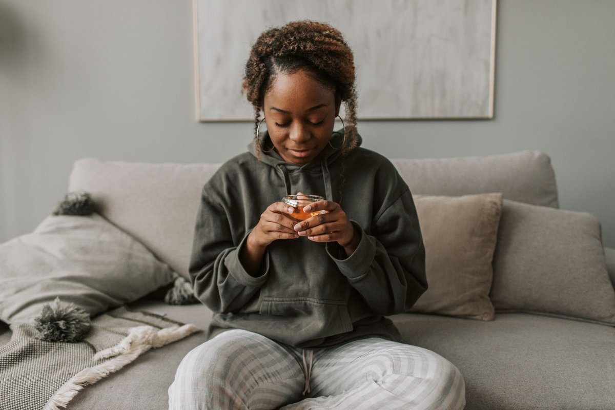 Woman sitting on a sofa holding a glass cup of tea and taking a quiet break