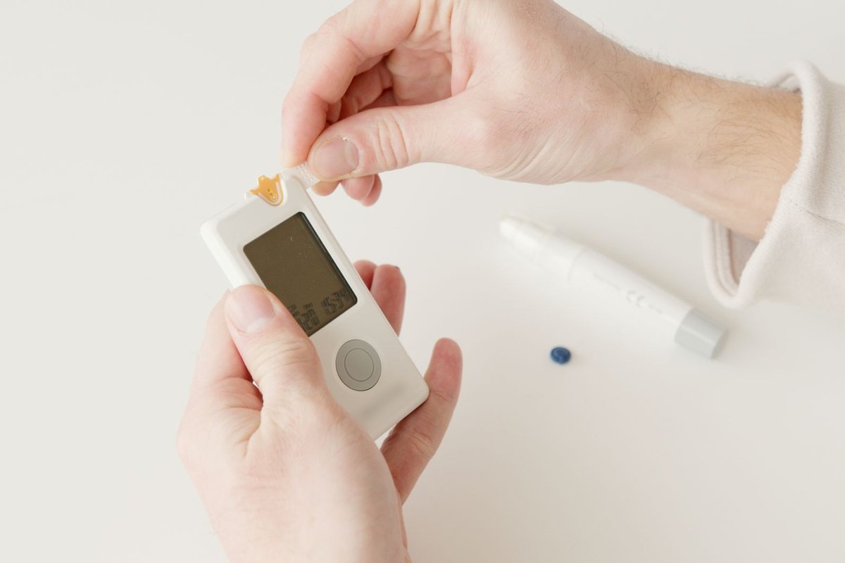 Hands holding a blood glucose meter with a test strip and a lancing pen nearby