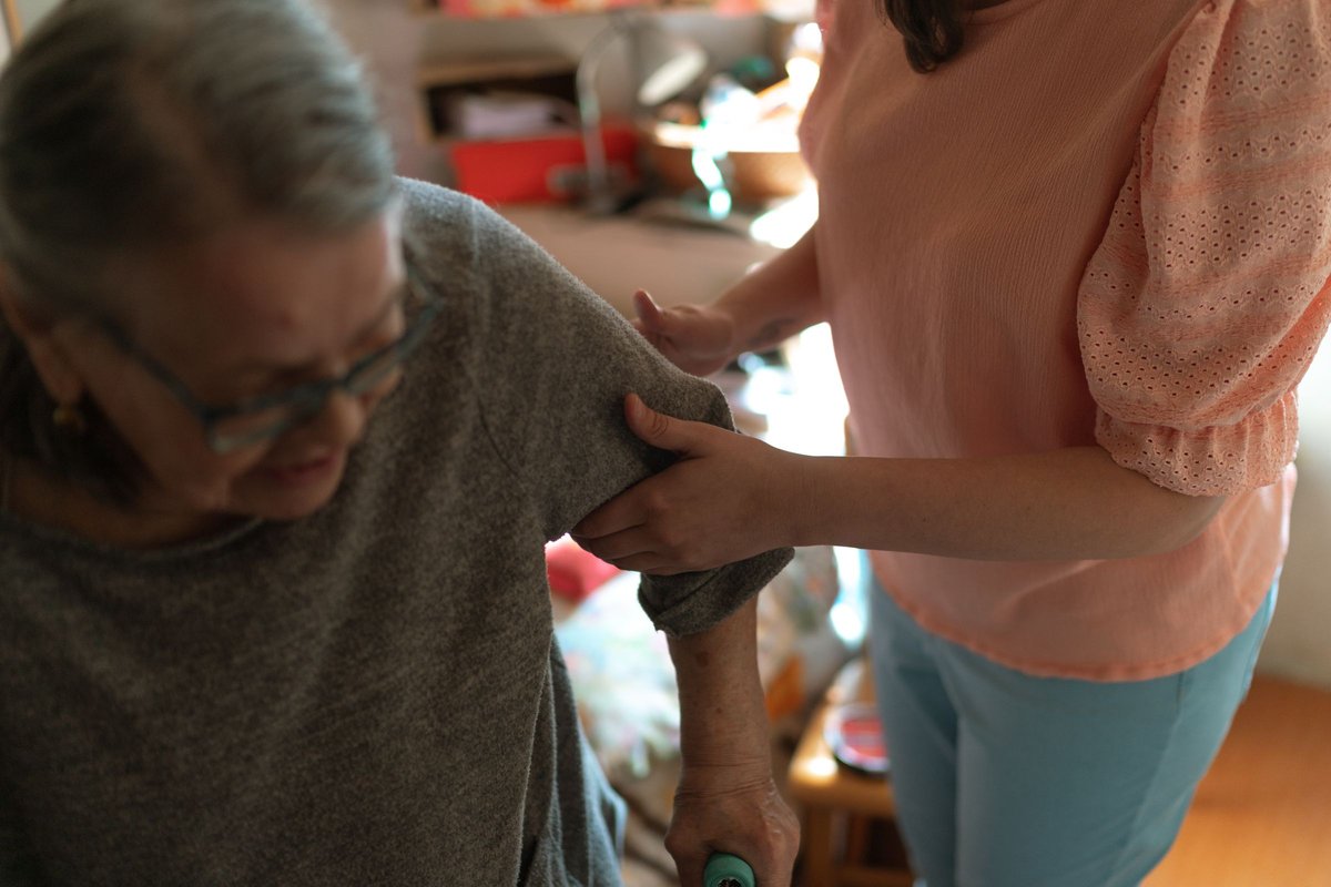 Caregiver steadying an older woman who holds a walking aid in her home