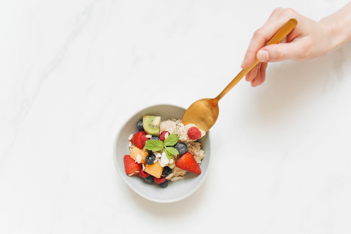 Bowl of oatmeal topped with berries, kiwi and almonds with a hand holding a spoon