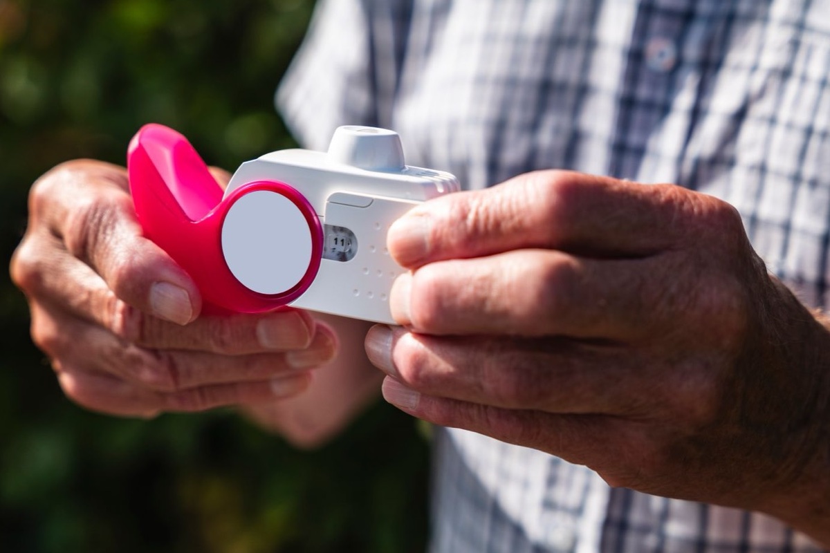 Older person's hands holding a pink and white inhaler outdoors