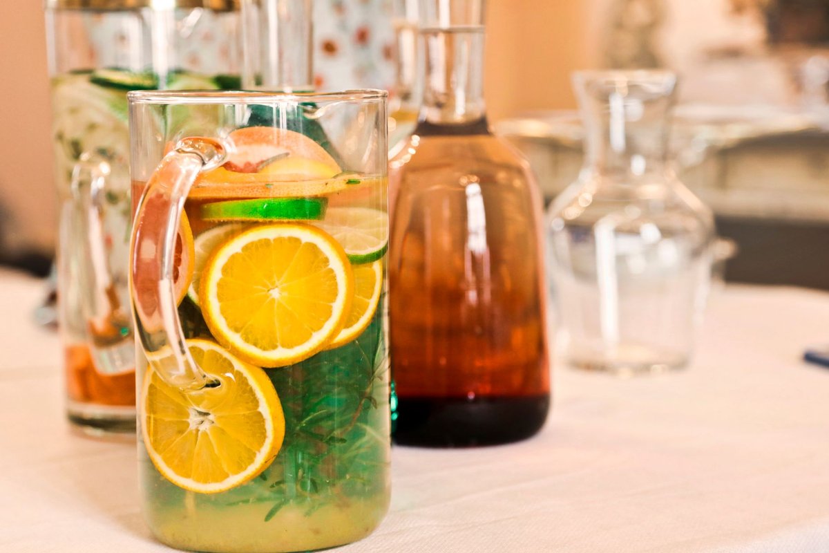 Glass pitchers of water with orange and lime slices and herbs on a table