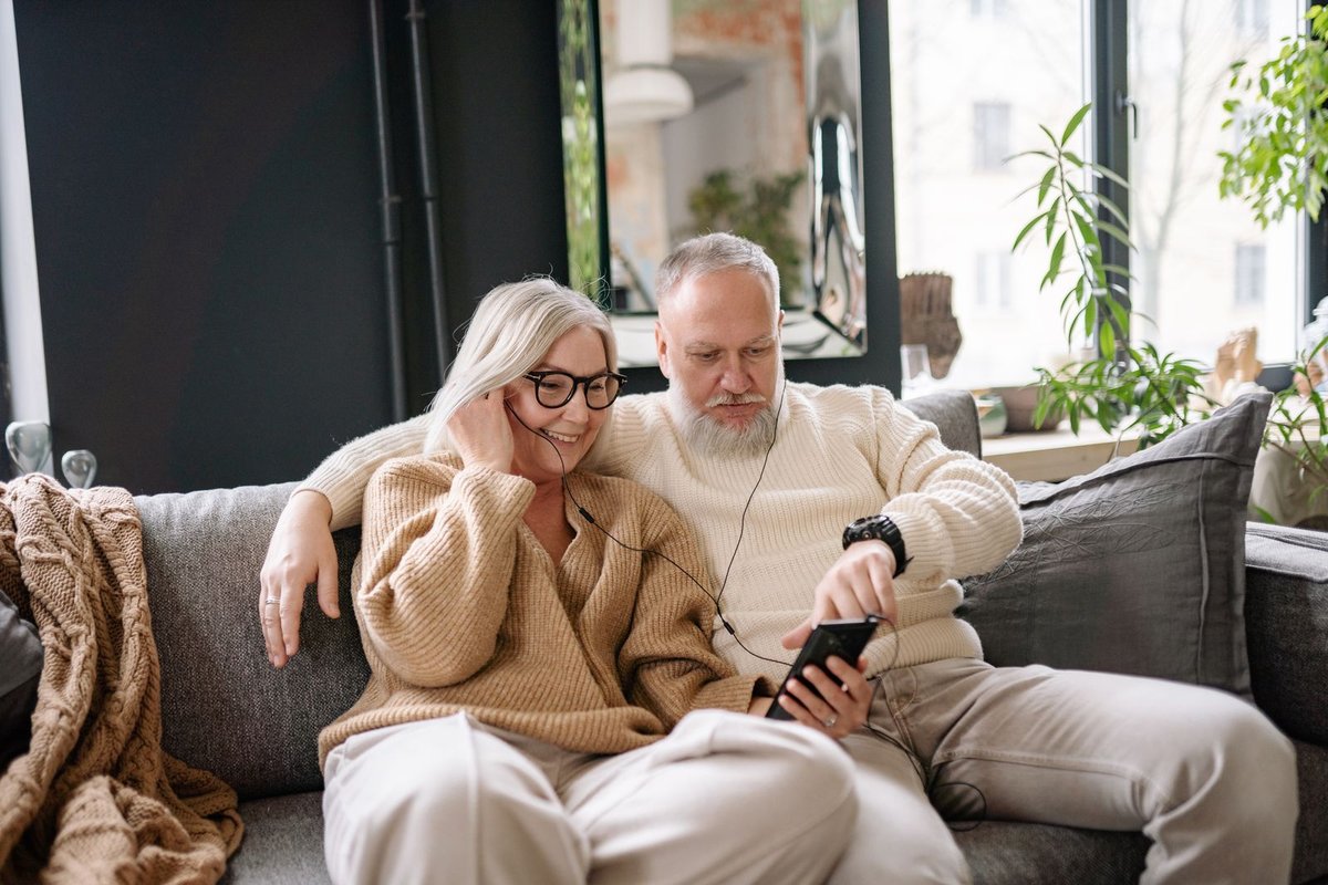Older couple sharing earphones and listening to music together on a sofa