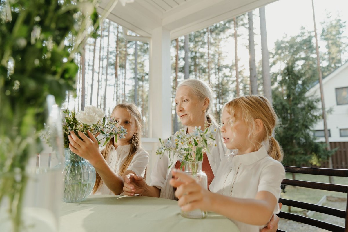 Grandmother and two girls arranging small flower bouquets together on a sunny porch
