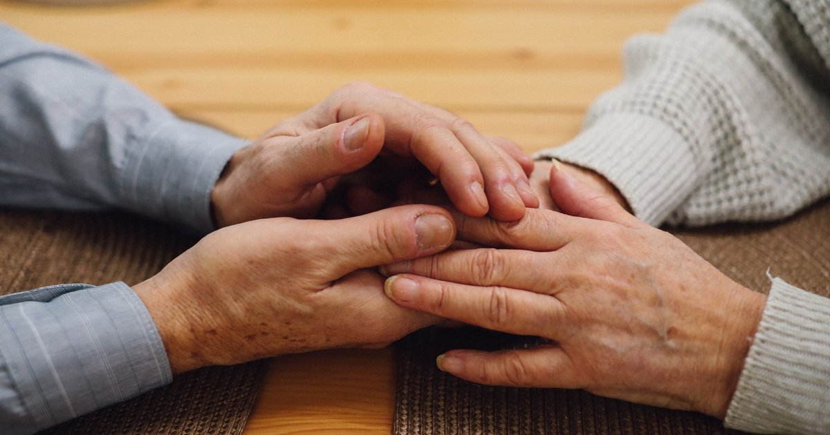 Two older people's hands held together over a wooden table