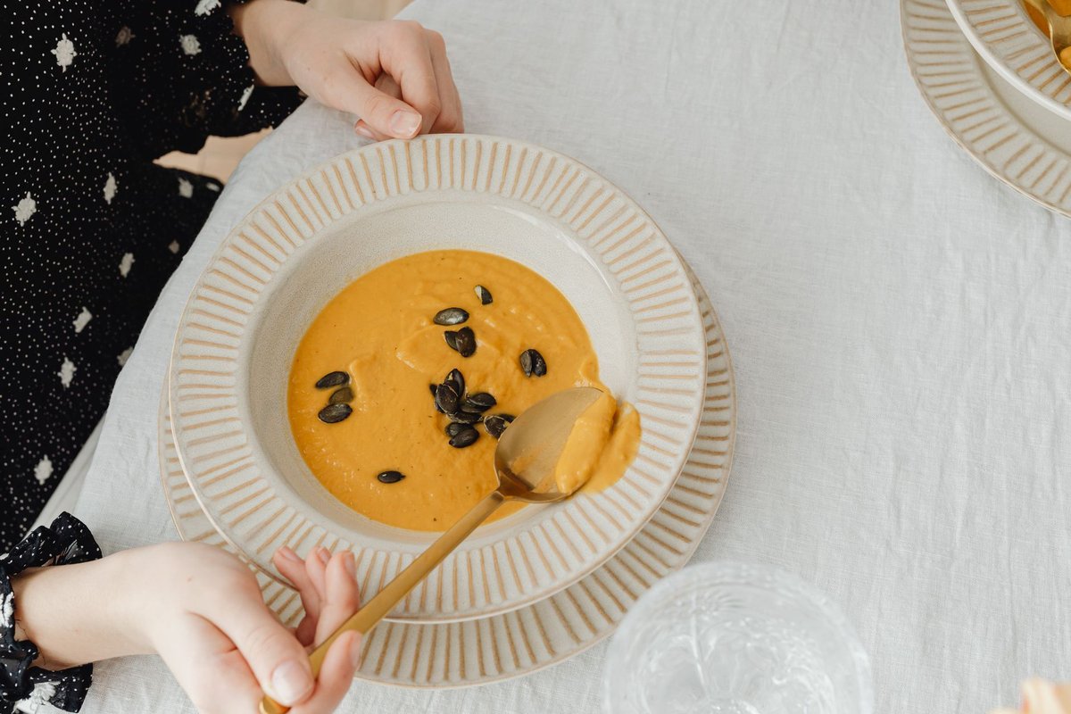 Smooth pumpkin soup in a ceramic bowl with a spoon resting in it on a linen tablecloth