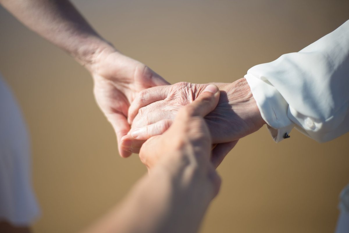 Younger hands gently holding an older person's hand, a sign of support for an at-risk senior