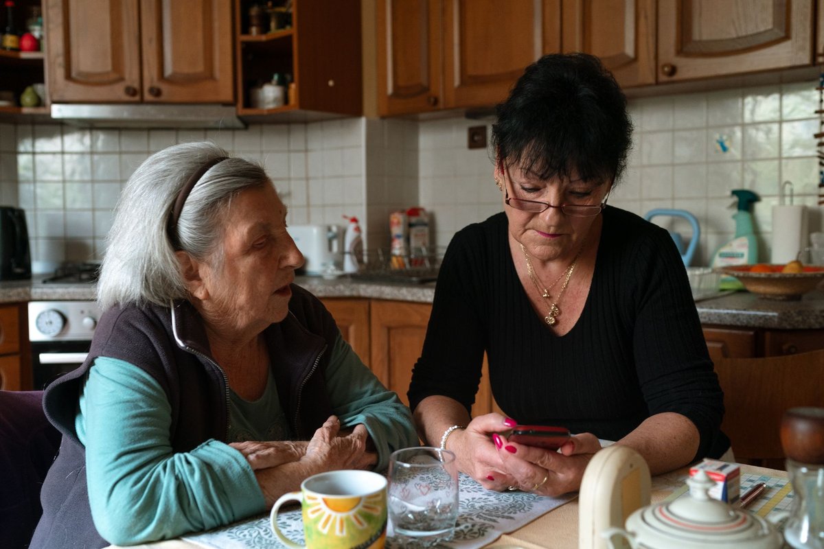 Home caregiver sitting with an older woman at her kitchen table, talking calmly together