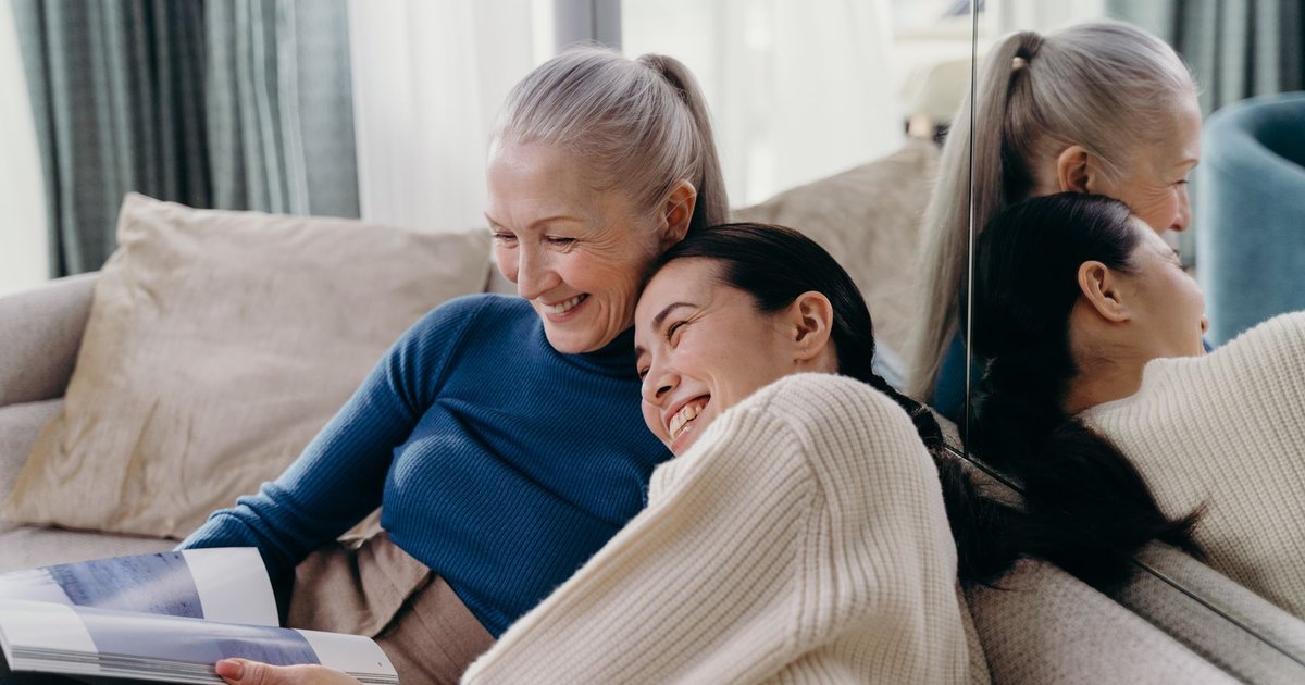 Older woman and her adult daughter smiling together on a sofa at home