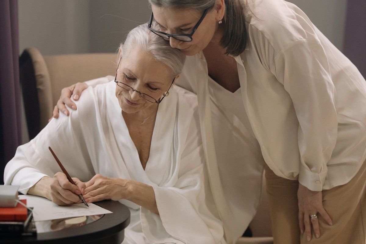 Older woman signing a form while a family member leans in to support her