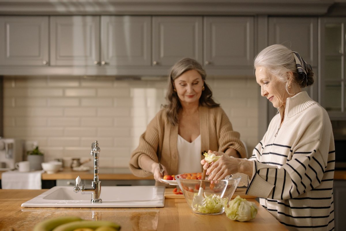 Two older women prepare a fresh salad with tomatoes together in a bright kitchen