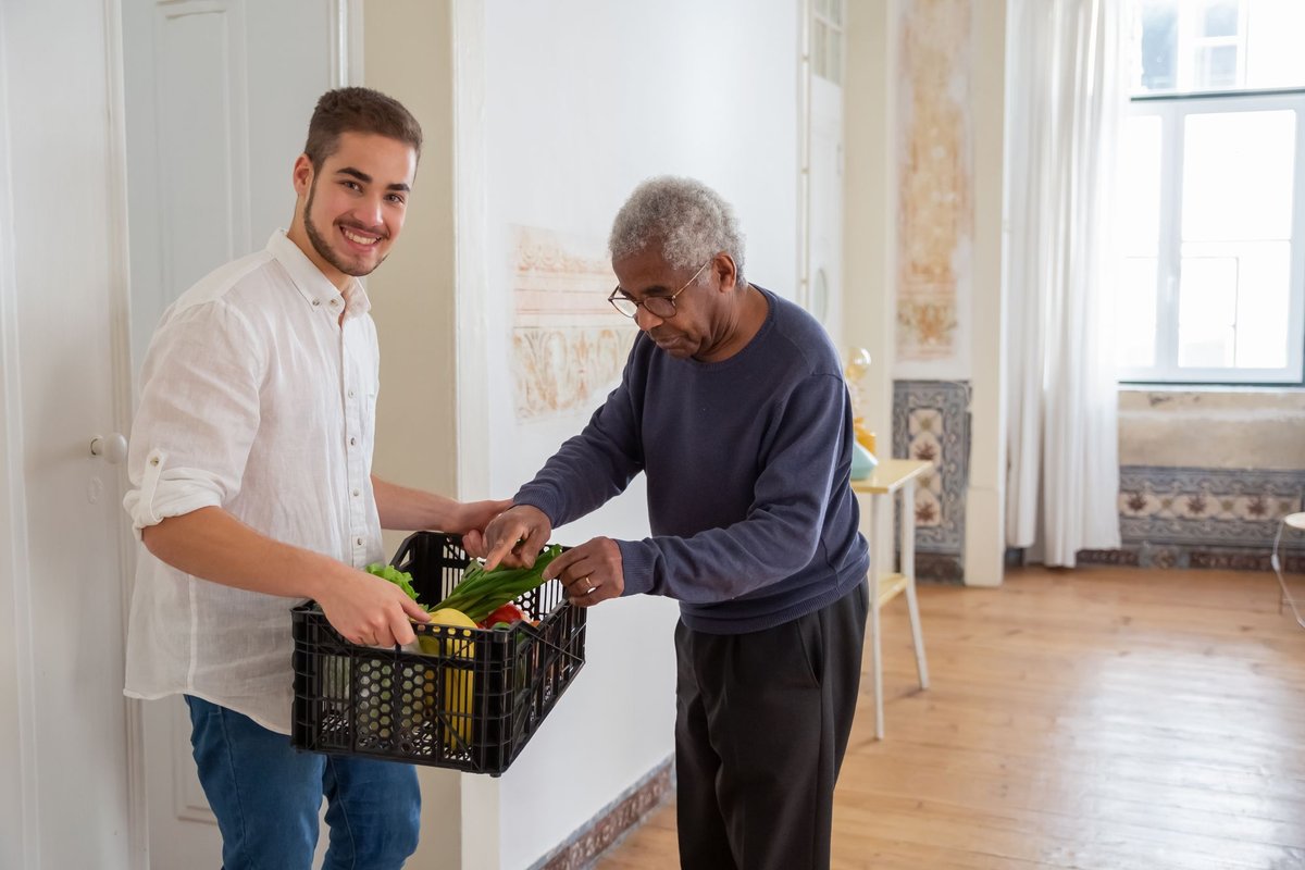 Smiling young man carries a crate of vegetables while an older man looks inside