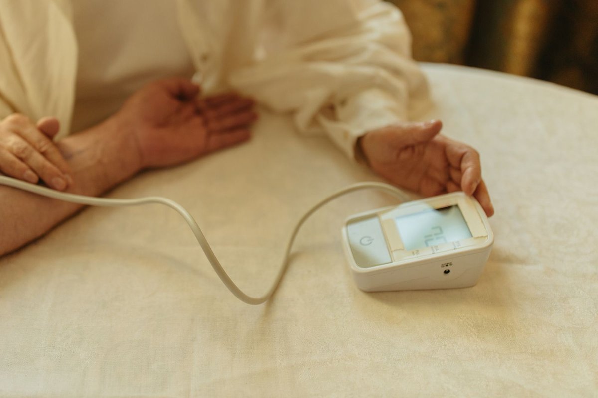 Hands resting on a table beside a home blood pressure monitor with a cuff cable