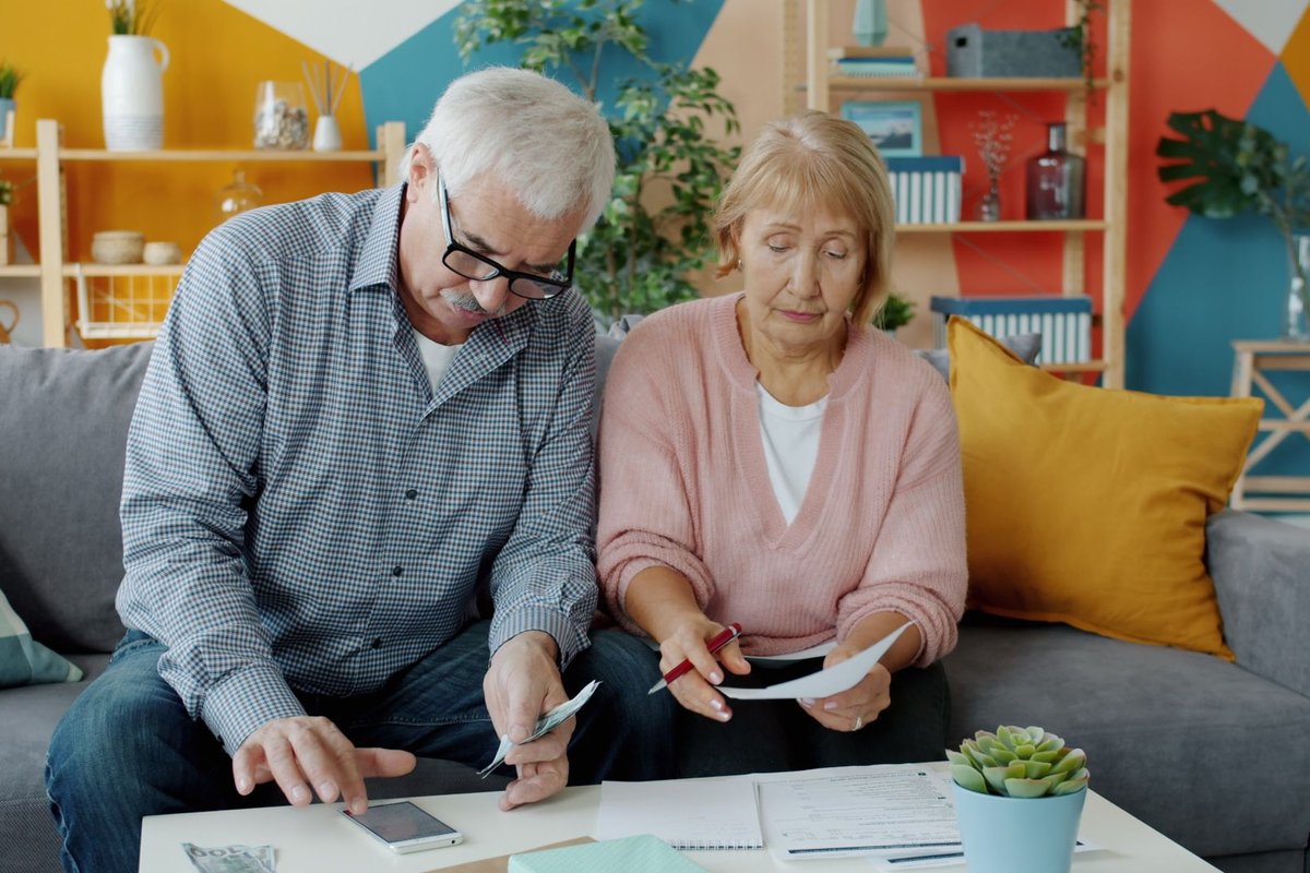 Older couple sitting on a sofa going through bills and papers together