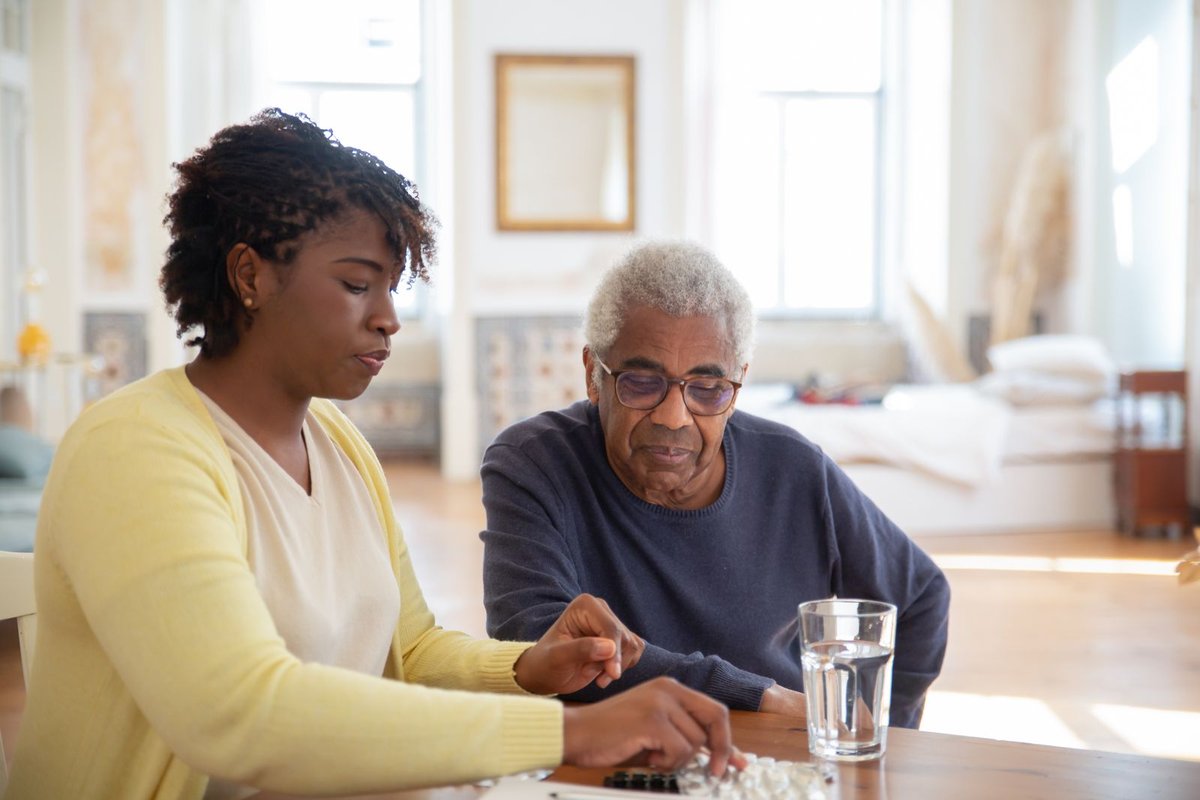Caregiver and older man sitting at a table going over daily pills with a glass of water