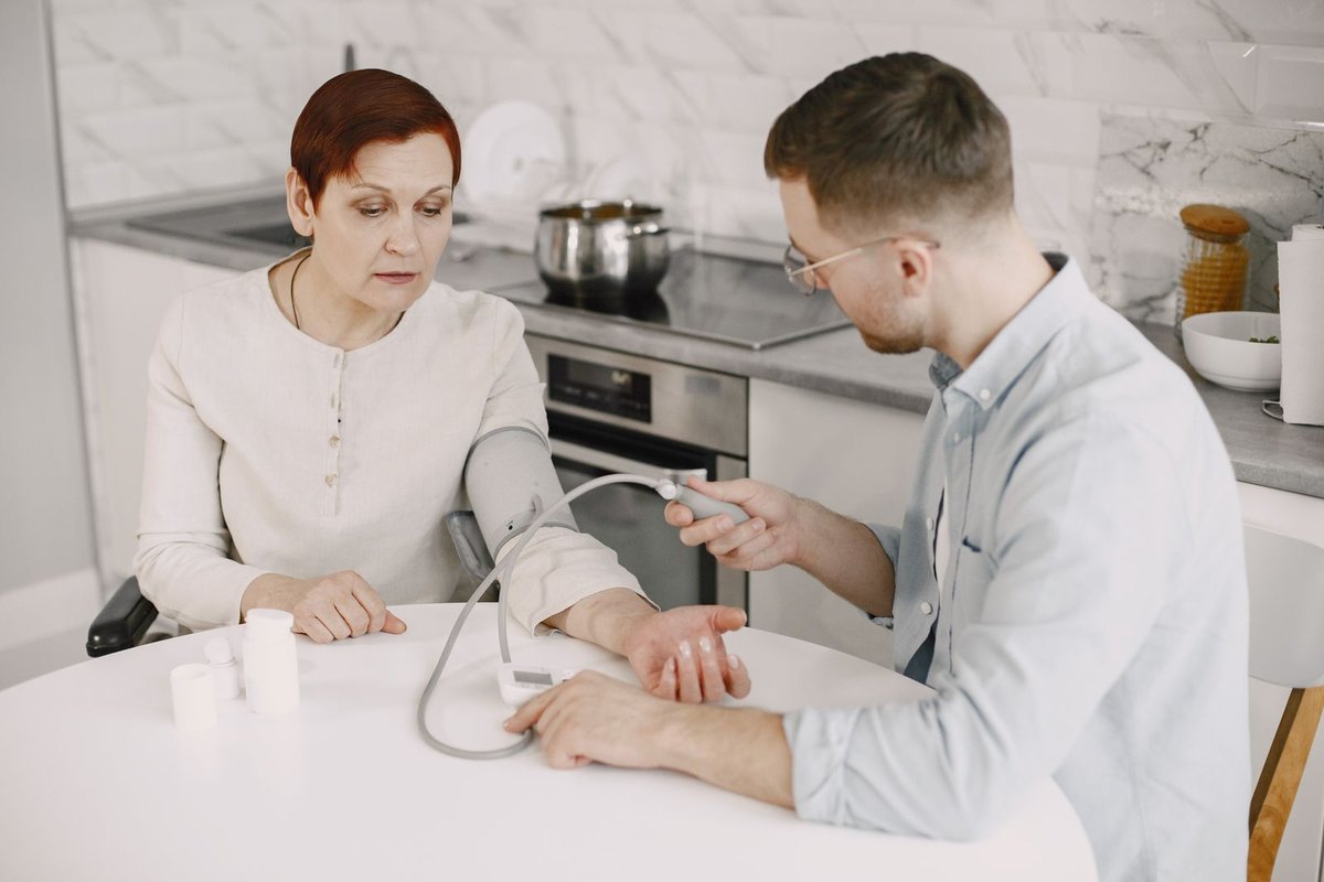 Helper taking a woman's blood pressure at a kitchen table with a home cuff