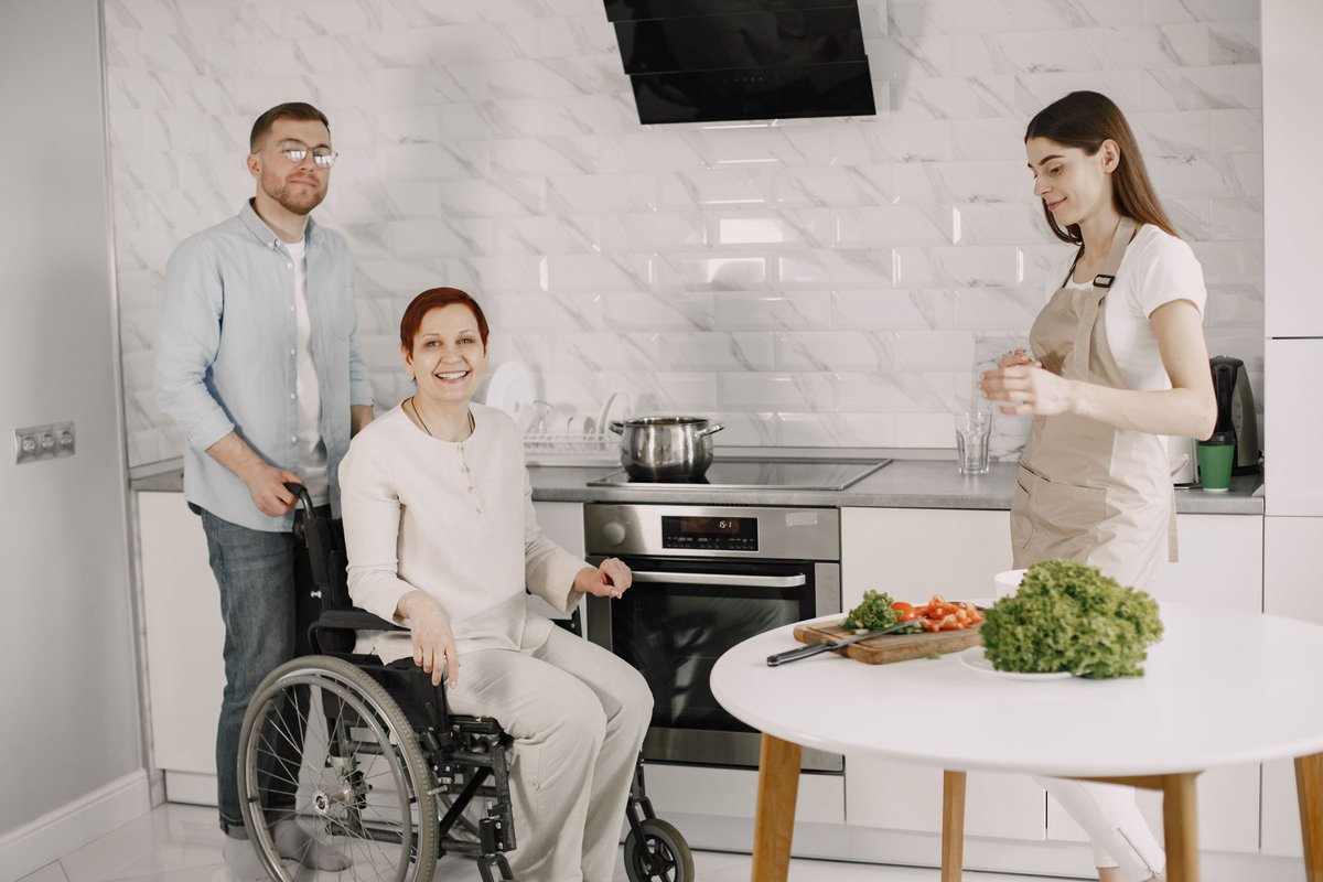 Smiling woman in a wheelchair in a bright kitchen with a man and a woman cooking