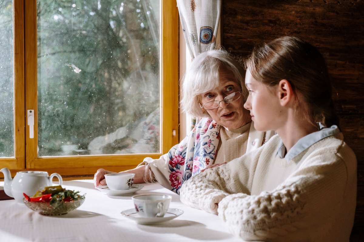Older woman and young woman talking over tea at a table by a window