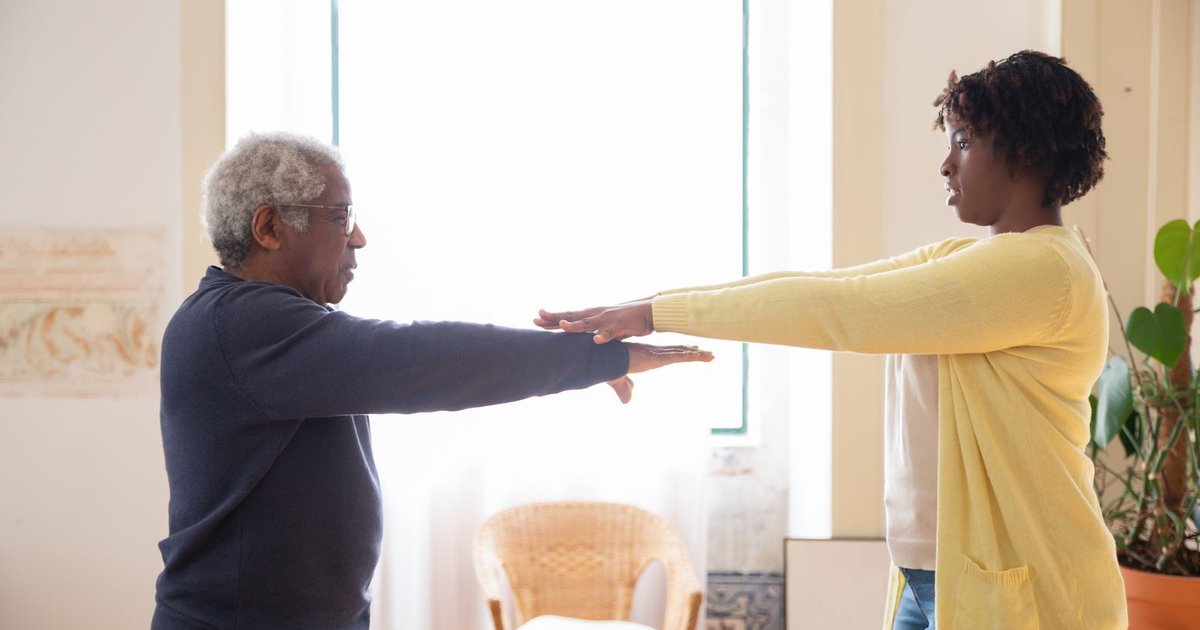 Older man and a young woman doing arm exercises together in a bright room