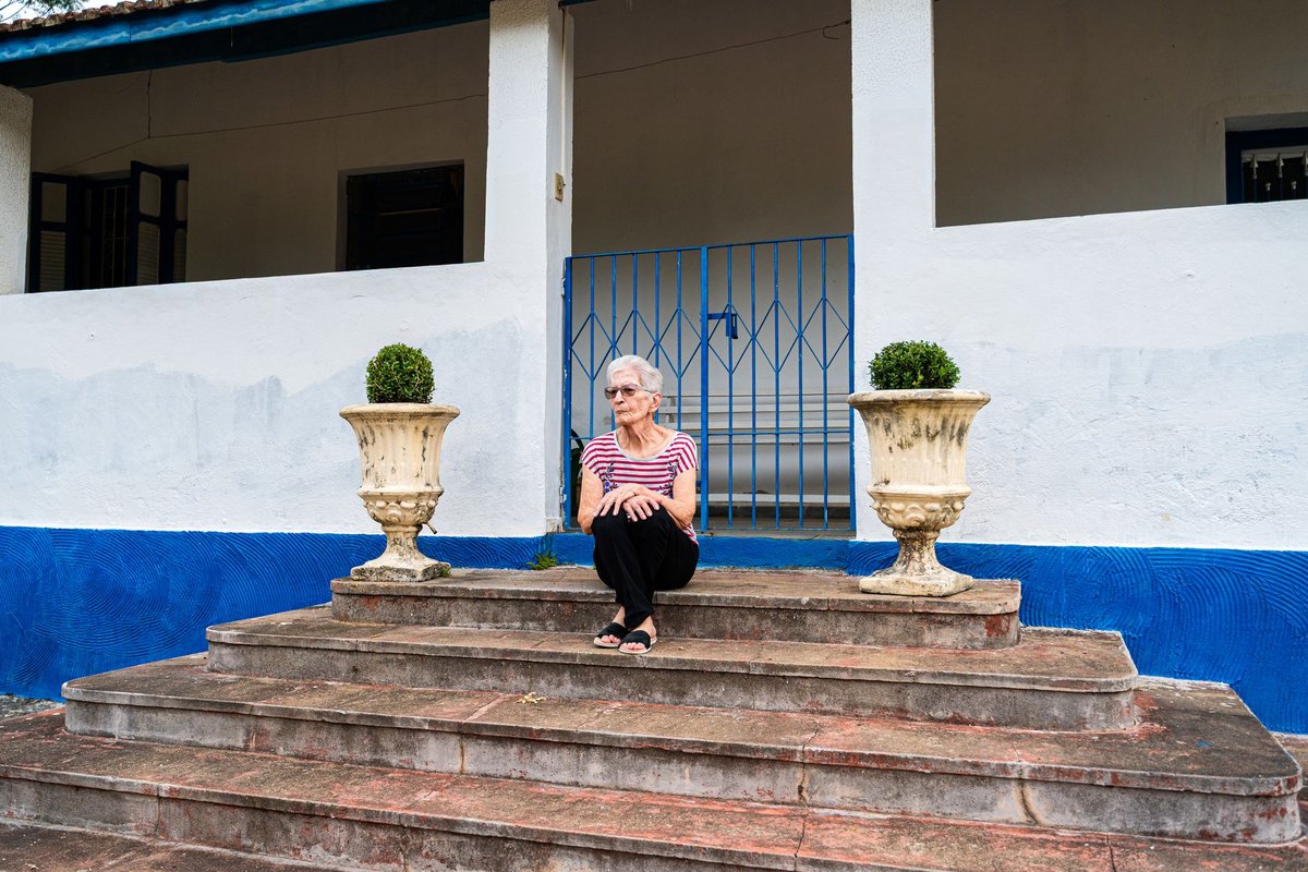 Older woman sitting on a wide set of stone steps in front of a house entrance
