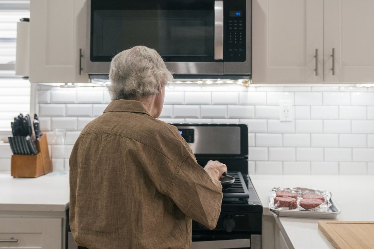 Older man with gray hair cooking at a gas stove in a bright white kitchen