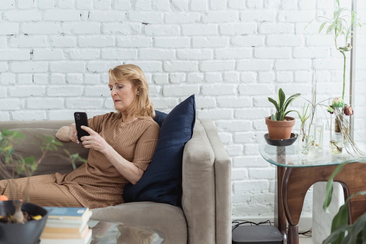 Woman with blond hair sitting on a gray sofa looking at her phone