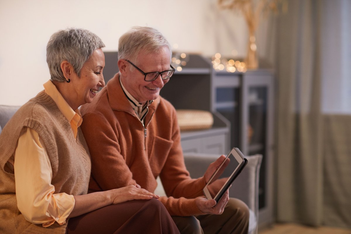 Smiling older couple sitting on a sofa looking at a tablet together
