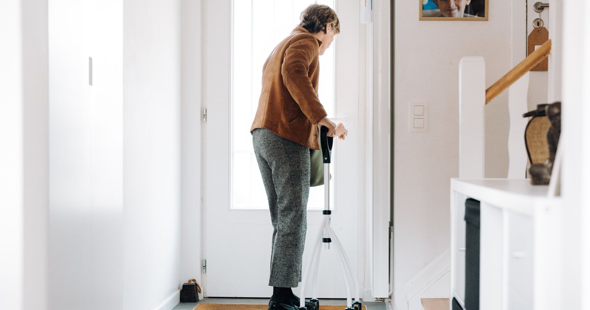 Older woman with a walker standing at the front door of a bright hallway at home
