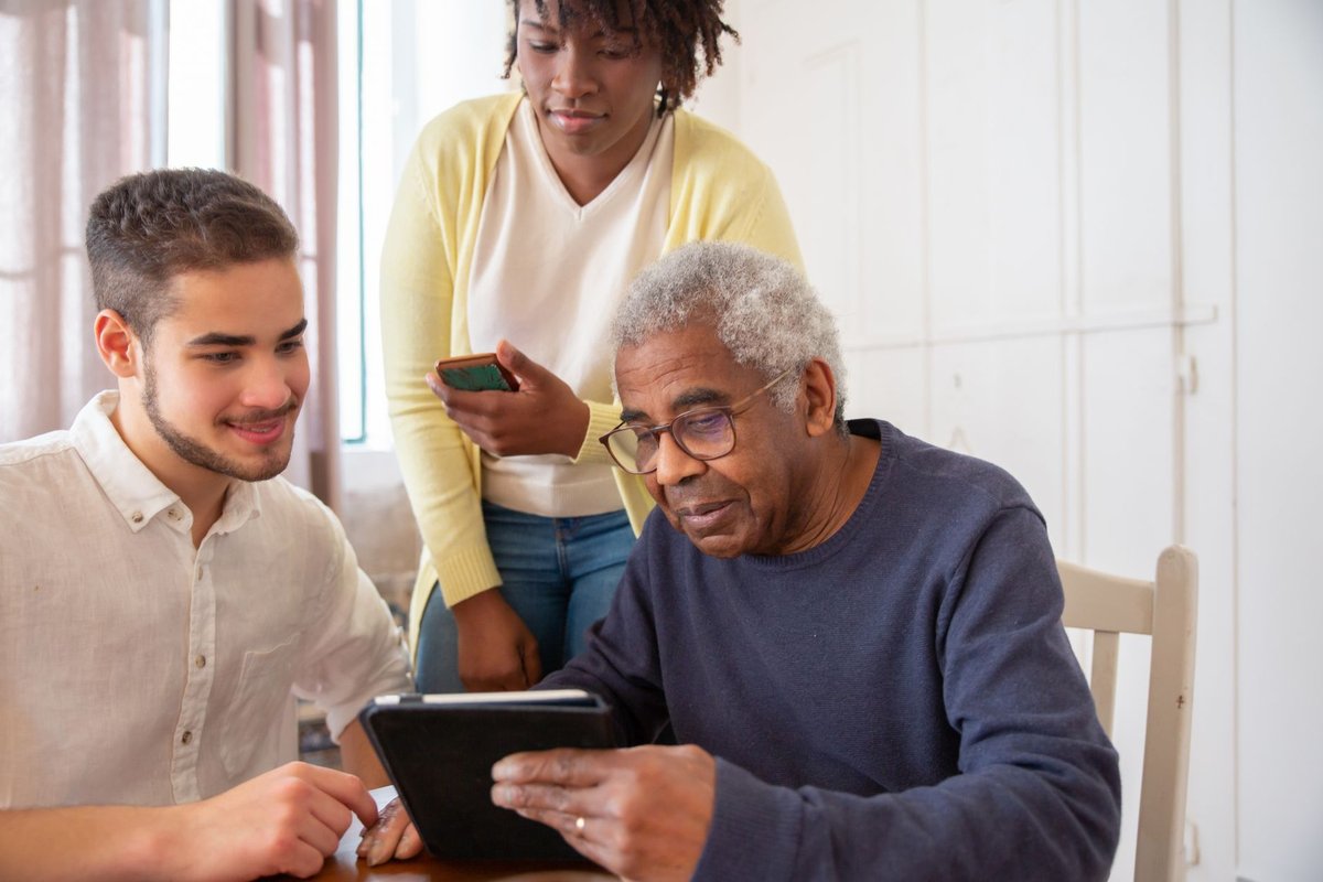 Older man looks at a tablet while a young man and a woman watch