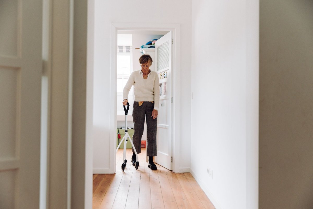 Older woman with a quad cane walking through a bright, clear hallway at home