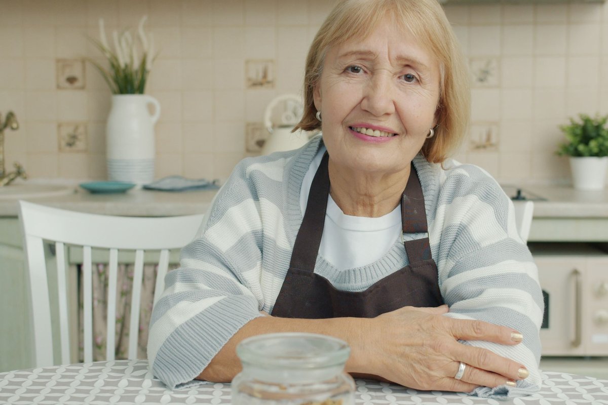 Smiling older woman in an apron sitting at a kitchen table