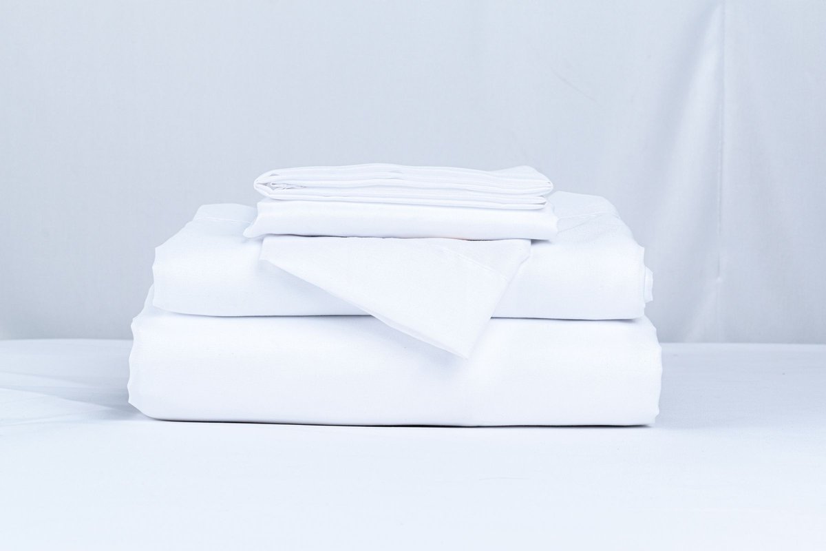 Stack of clean white folded bed linens on a light surface