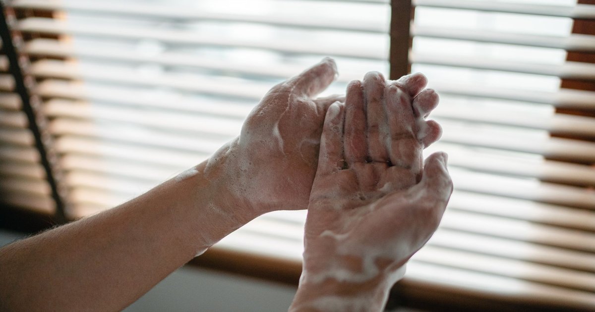 Close-up of soapy hands being washed in front of a sunlit window blind